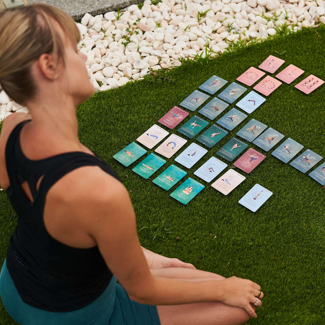 A woman sitting on the grass beside a sequence of Yoga Deck cards
