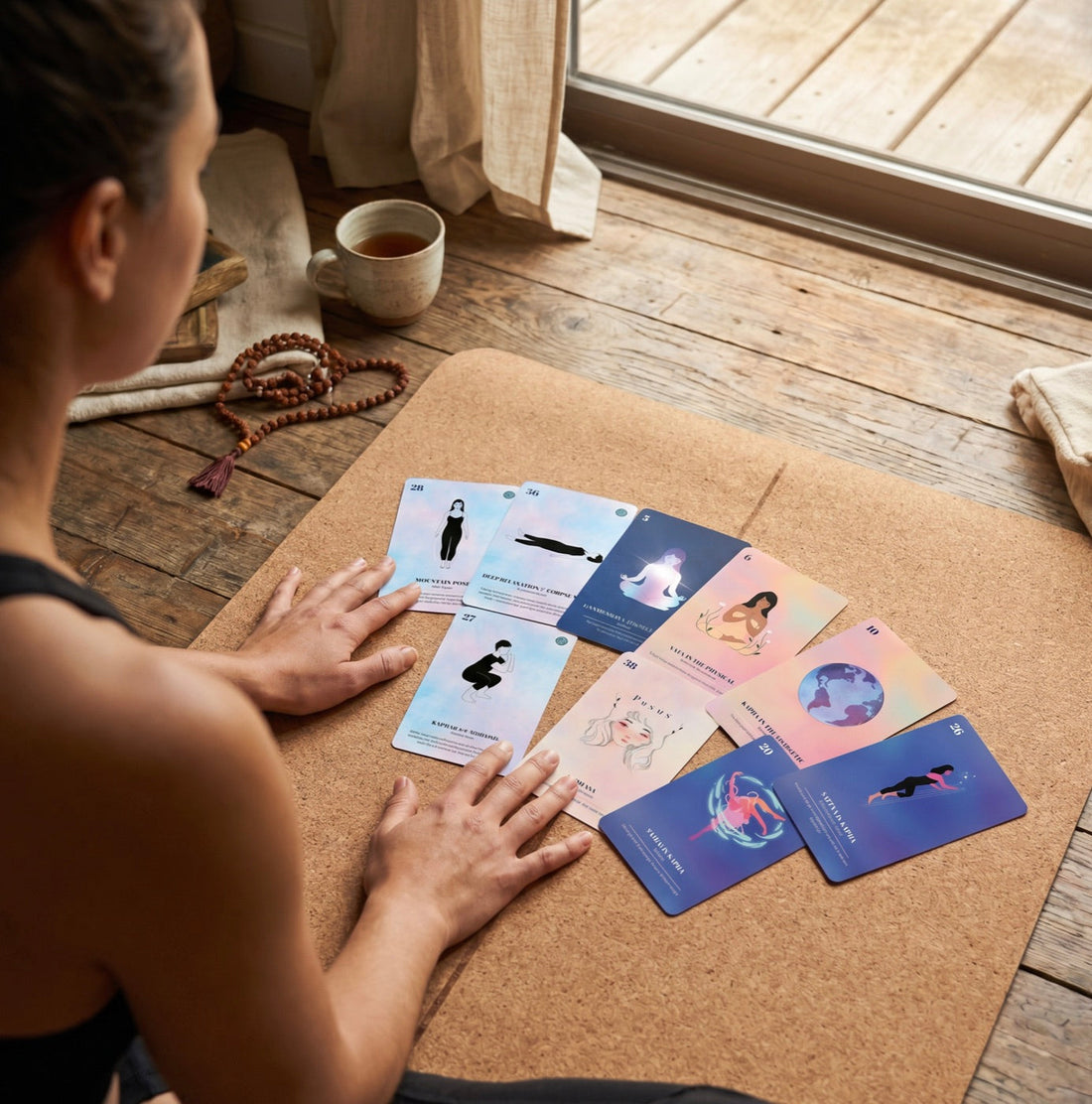 A practitioner laying out a spread of cards on a cork mat beside a cup of tea